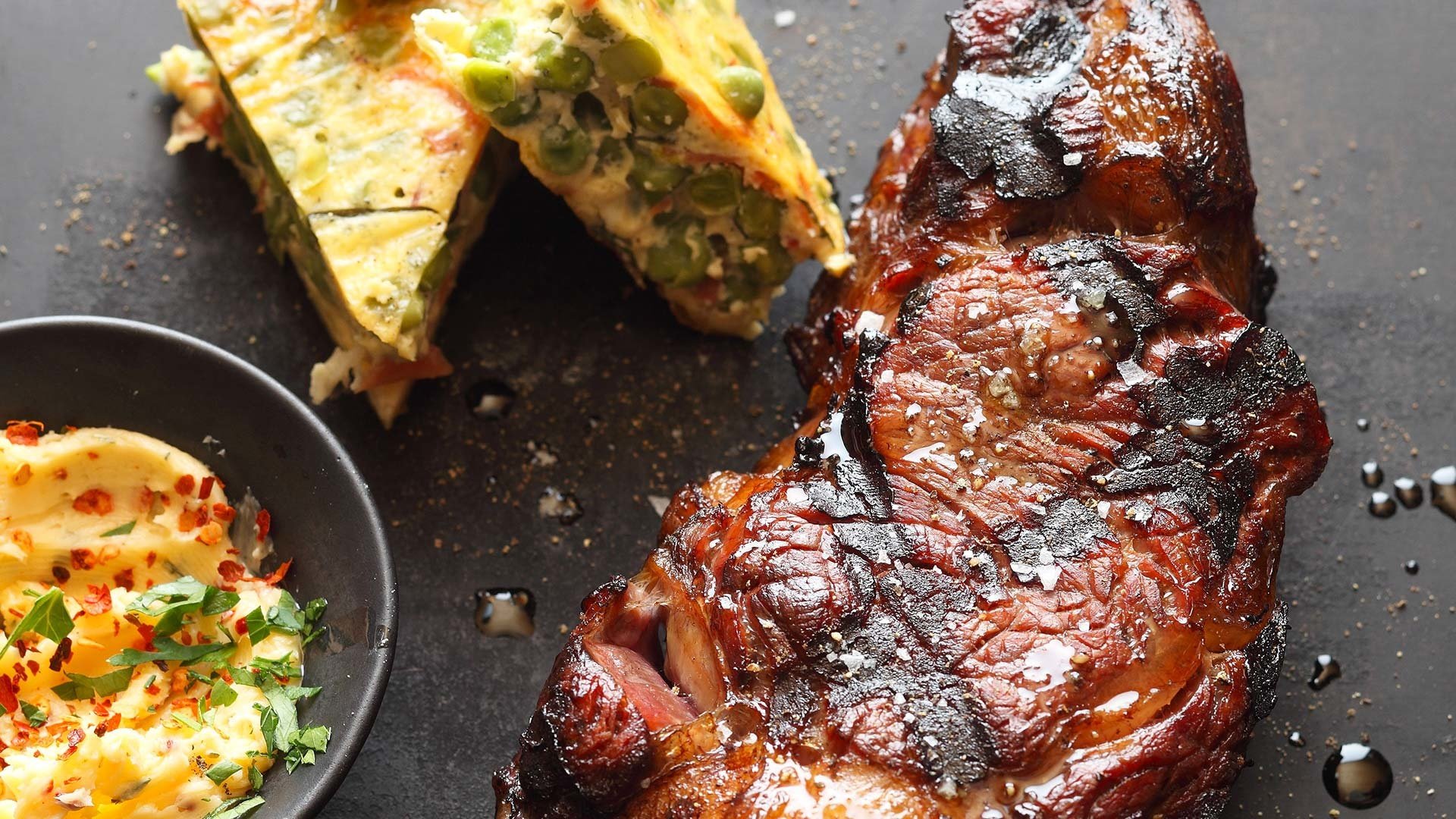  Tranchen vom One-Pound US Nebraska Steak, serviert mit Chili-Kräuter-Butter, Erbsen-Fritatta mit Parmaschinken und Basilikum


